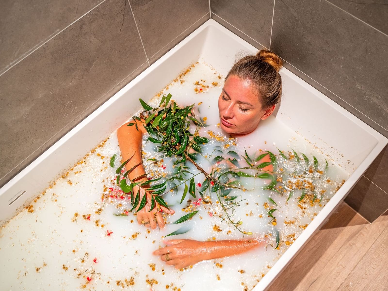 Person relaxing in a bubble-filled bathtub adorned with greenery and flower petals in The Rock Spa at Golden Rock Resort
